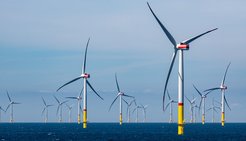 View over the sea with the wind turbines of an offshore wind farm staggered at a great distance to the horizon.